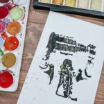 watercolor and ink painting featuring black brushstrokes and splatters on white paper with gold metallic accents, abstract gestural marks creating a sense of movement and layering